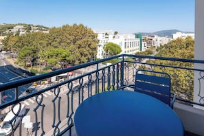 A balcony with a view of a city street, a blue table, and a metal railing. - Hôtel Magnan (Nice)
