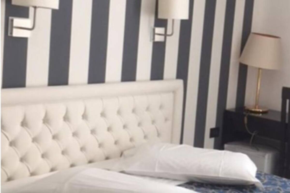 Un dormitorio con cabecera capitonada, una mesita de noche con lámpara y una silla.
