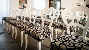 A row of white chairs with patterned cushions in a room with a tiled floor, a poster on the wall, and a chandelier. - Hotel Centrale Trieste (Trieste)