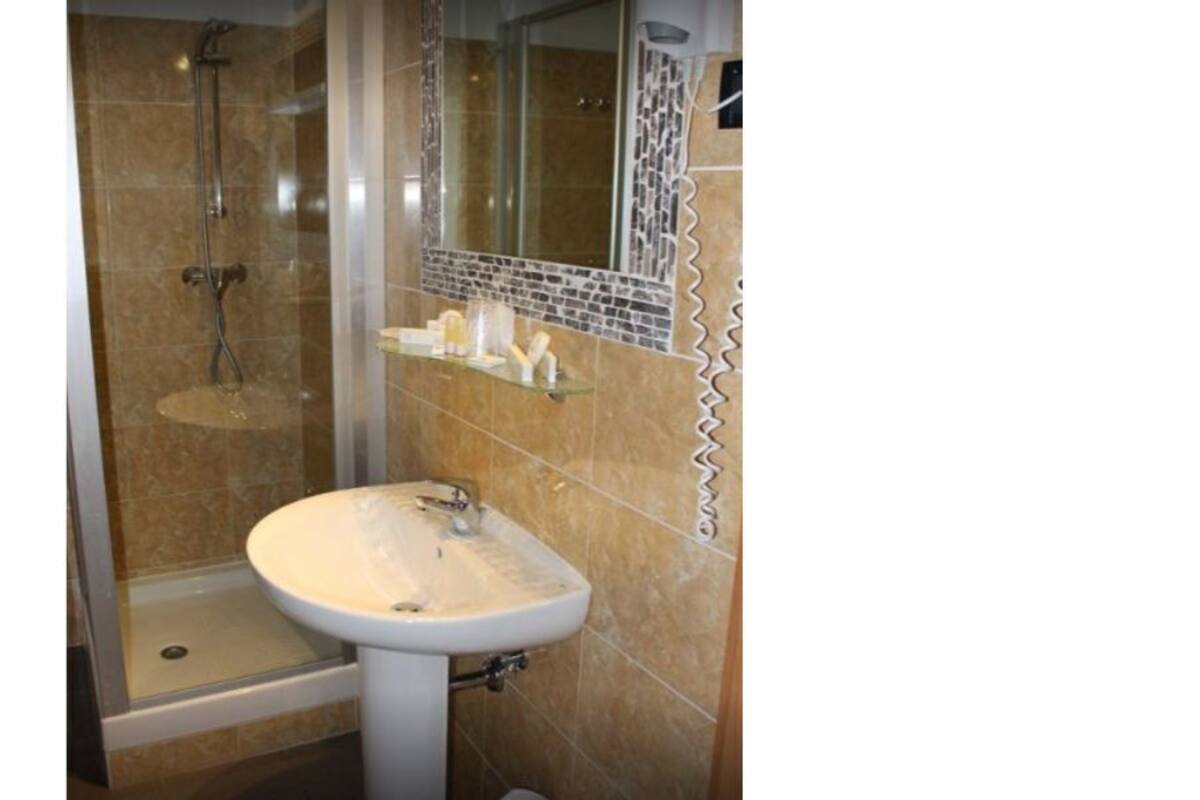 Baño con lavamanos, ducha y estante de vidrio con artículos de aseo.
