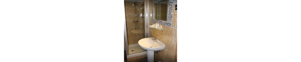 A bathroom with a sink, shower, and a glass shelf with toiletries.