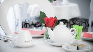A table set with white teacups, a teapot, a glass with a red rose, and green napkin holders. - Hotel Centrale Trieste (Trieste)