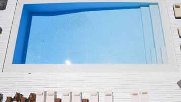 Una piscina rectangular con una terraza blanca alrededor.