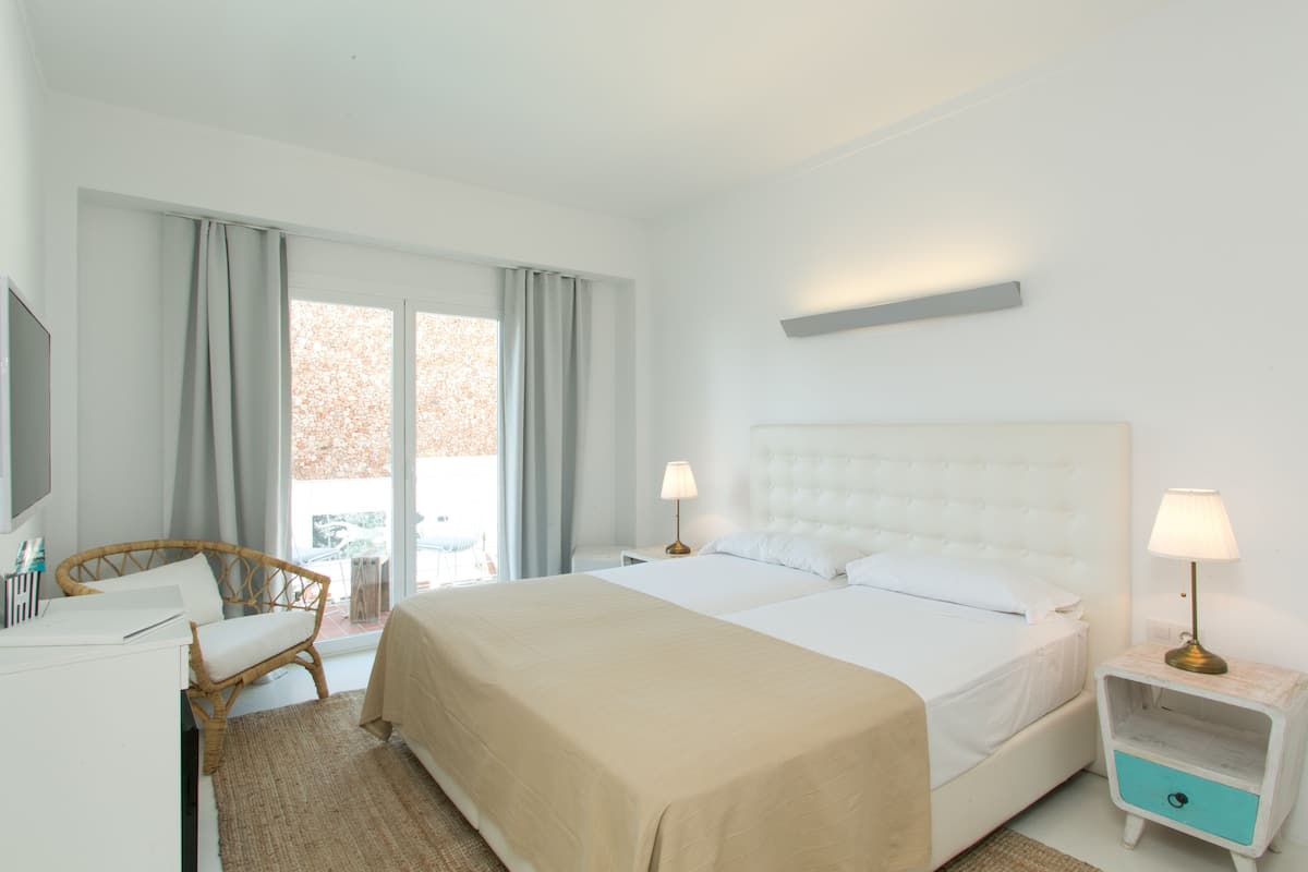 A hotel room with a large bed, two bedside tables with lamps, a chair, a desk, and a window with curtains.