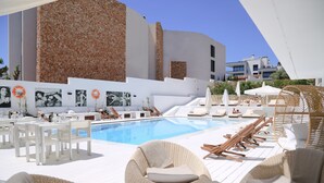 A poolside area with lounge chairs, a dining setup, and a modern building with a stone facade. - Zhero Hotel Mallorca (Calvia)