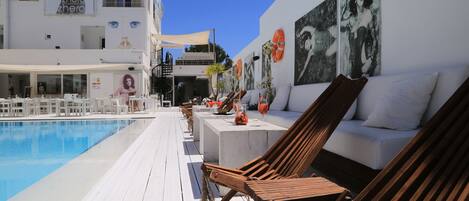 A poolside area with lounge chairs, a white pool, and artwork on the walls.