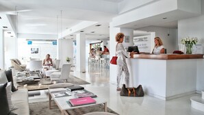 A modern hotel lobby with a reception desk, seating area, and a view of the street. - Zhero Hotel Mallorca (Calvia)