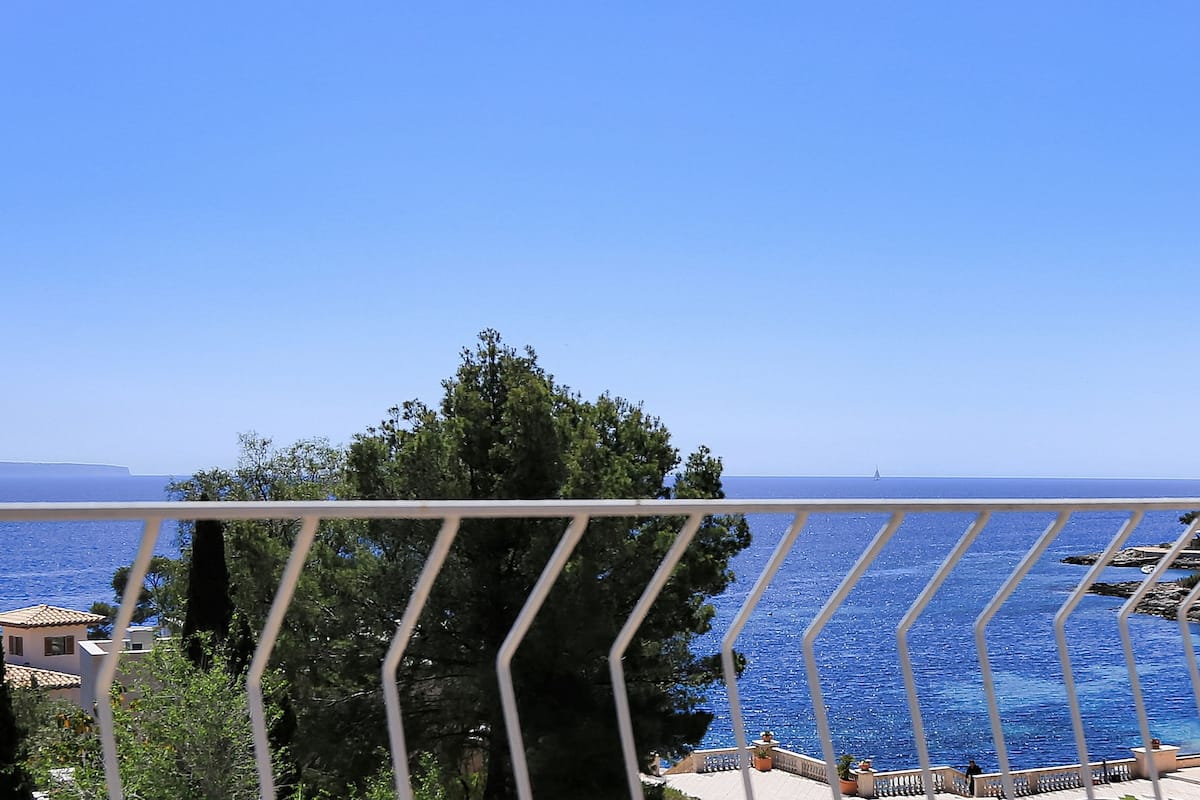 A balcony with a view of the sea and a distant sailboat.
