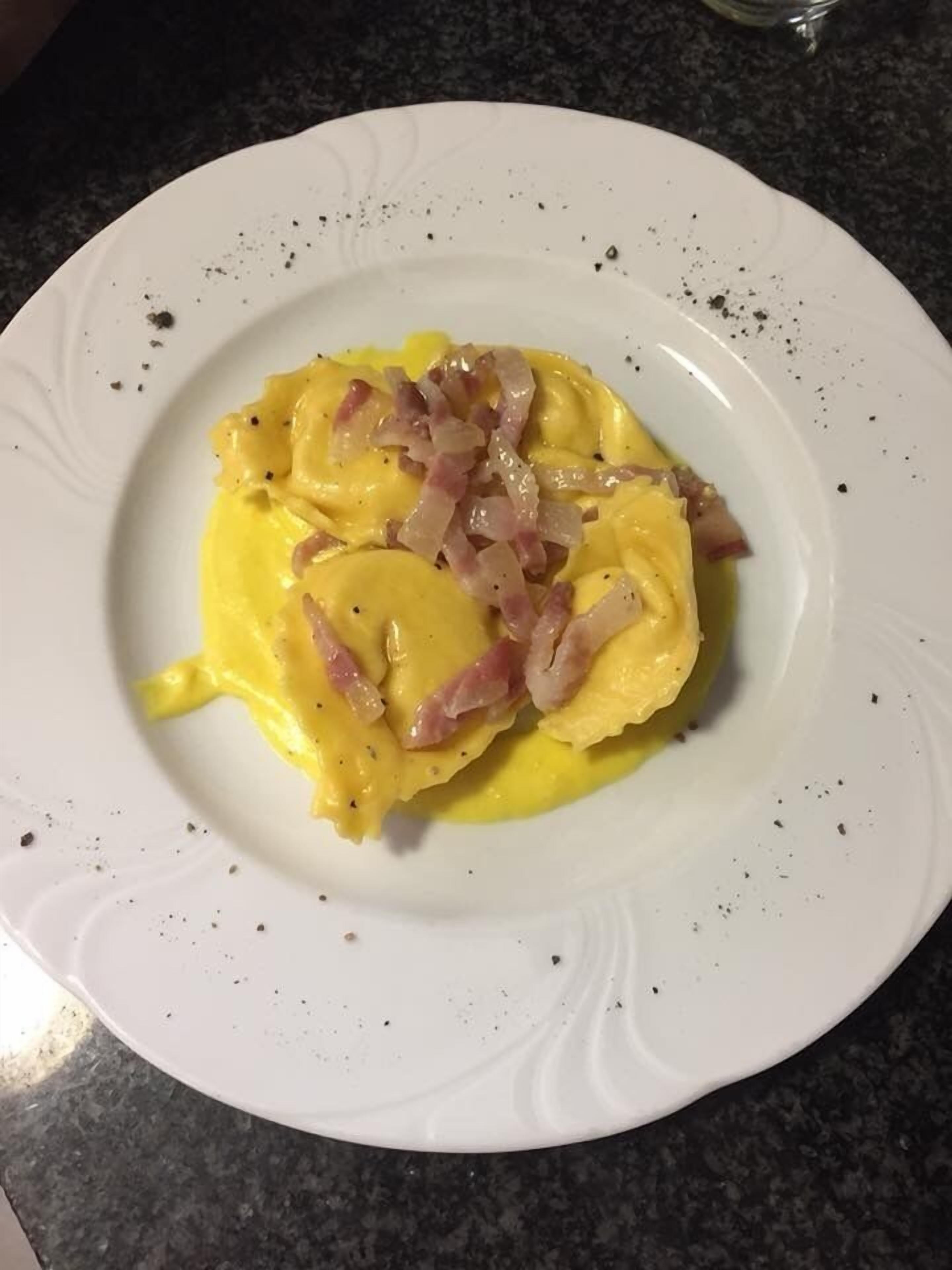 A white plate with a creamy yellow dish topped with bacon and onions, served on a dark granite countertop.