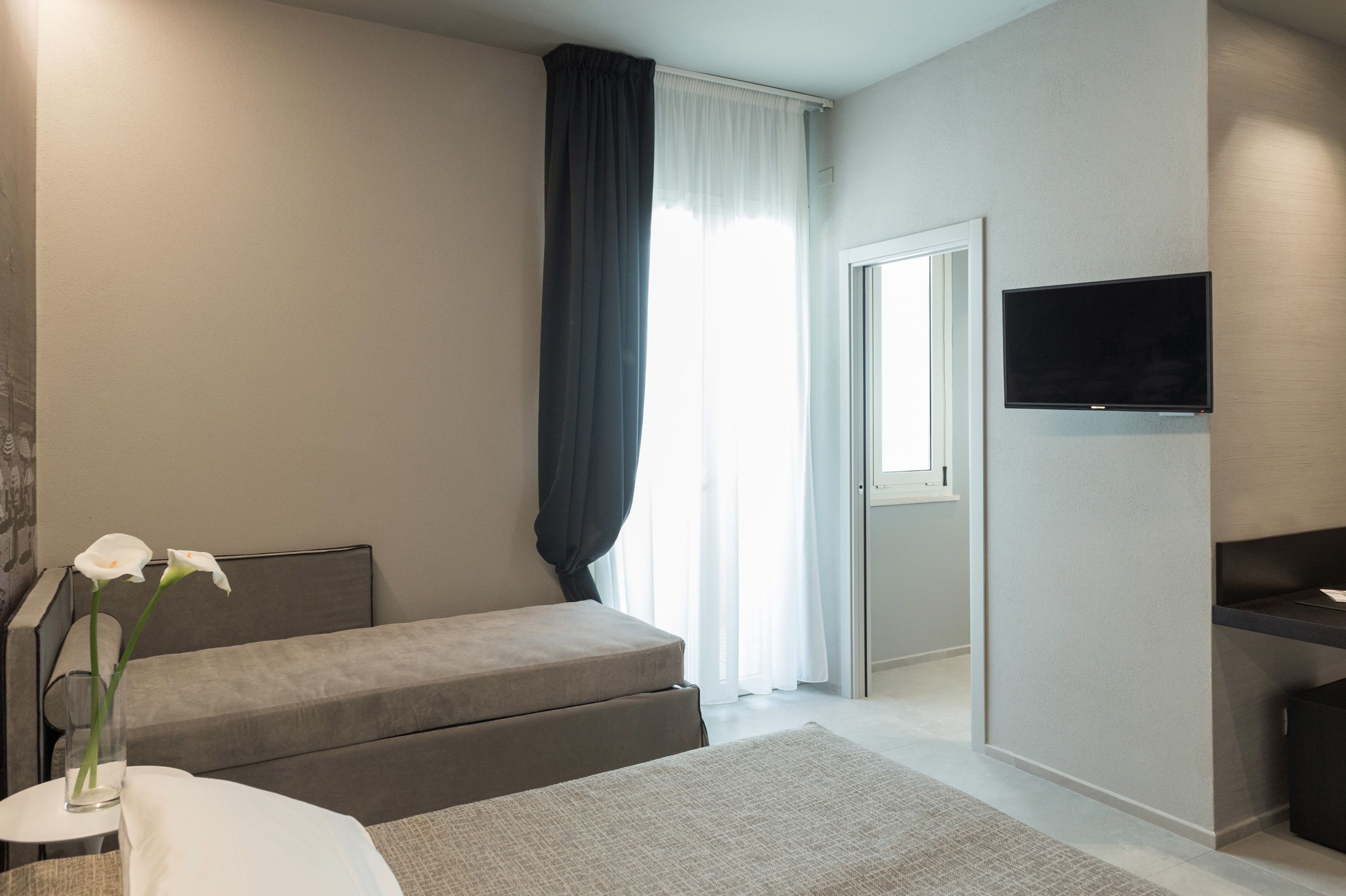 Quarto moderno com cama, mesa de cabeceira, televisão e janela com cortinas.