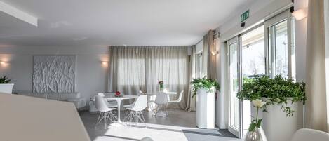 A modern hotel room with a dining area, large windows, and a potted plant.