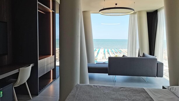 Une chambre d’hôtel moderne dotée d’une grande fenêtre donnant sur la plage et l’océan.