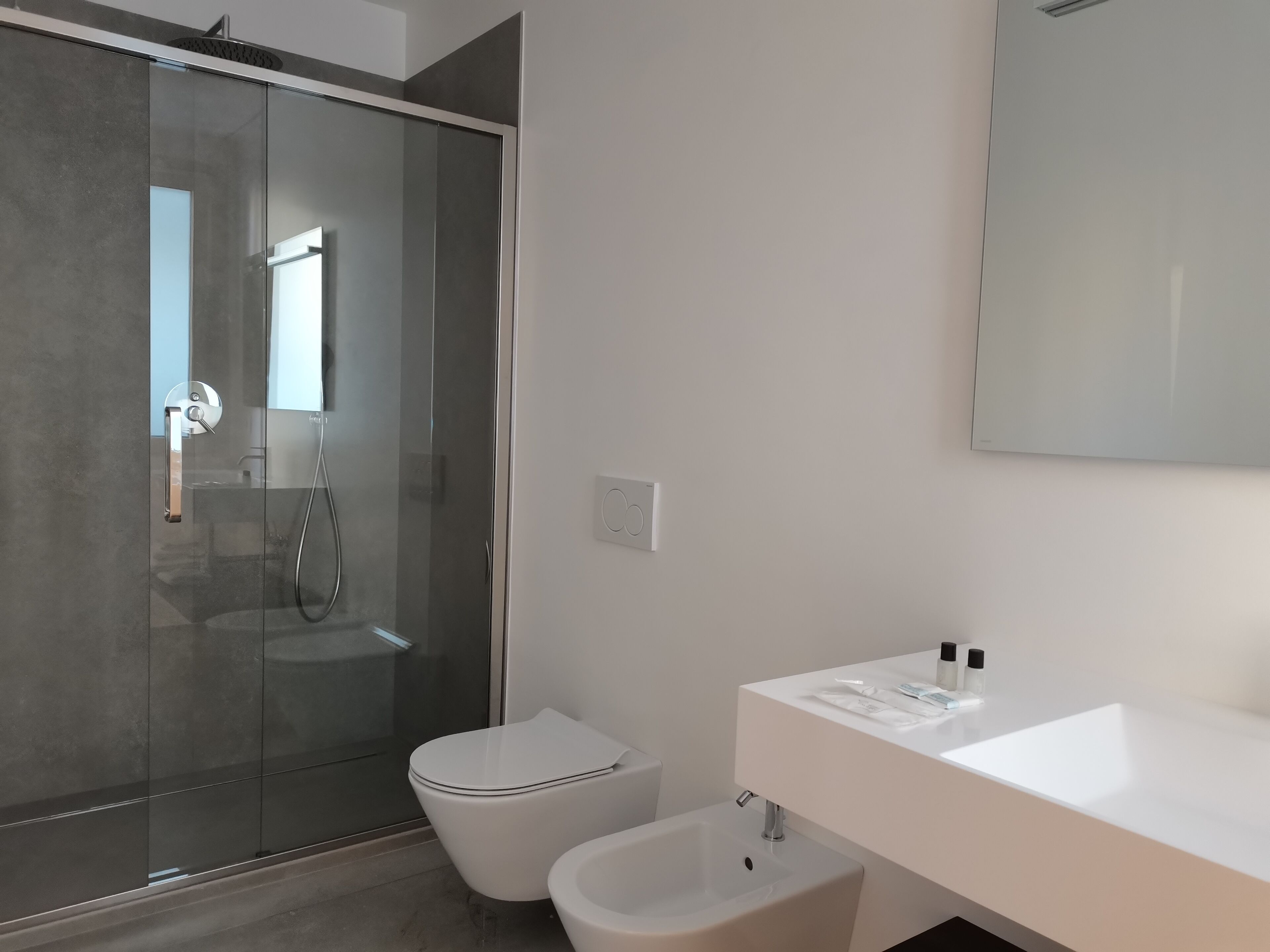 A modern bathroom with a glass-enclosed shower, a white toilet, and a white sink with a mirror above it.