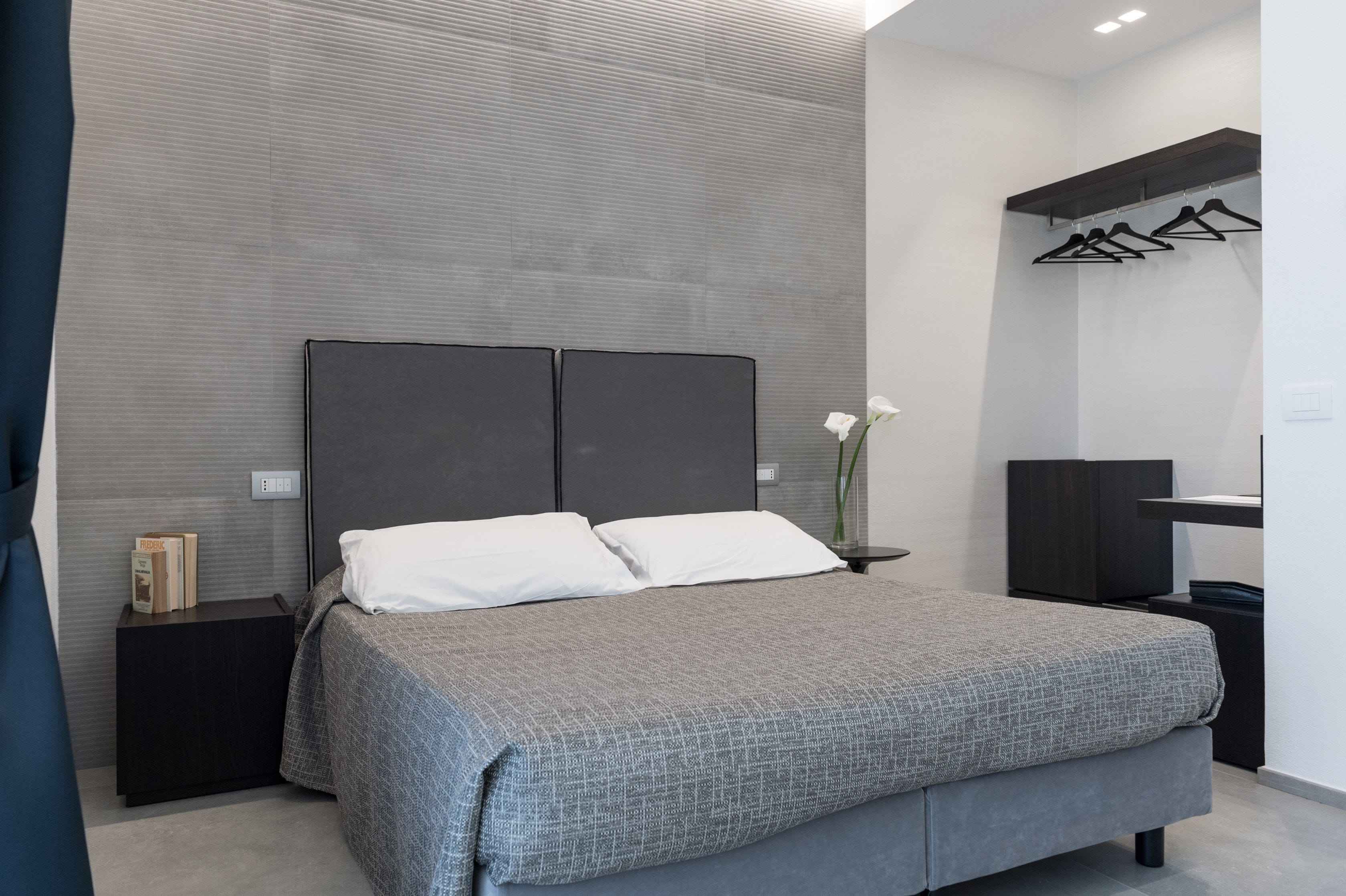 Une chambre à coucher moderne avec un lit gris, une table de chevet, une commode et un miroir.