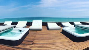 Une terrasse en bois avec quatre bains à remous et des chaises longues donnant sur un océan d’un bleu éclatant.