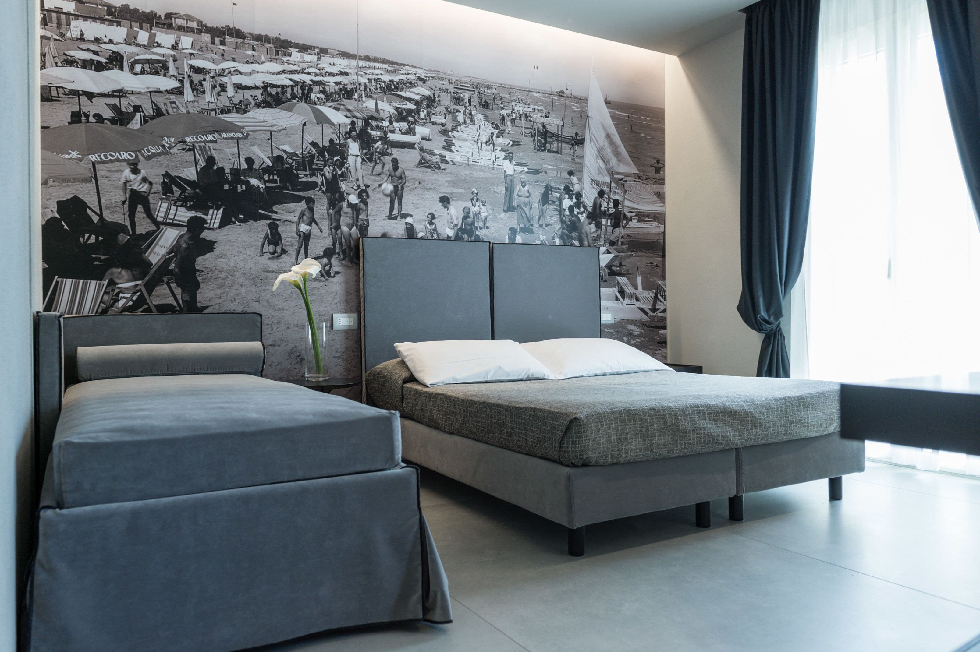 Una habitación de hotel moderna con una cama grande, una cama más pequeña y un mural en la pared que representa una playa.