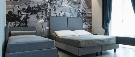 Una habitación de hotel moderna con una cama grande, una cama más pequeña y un mural en la pared que representa una playa.