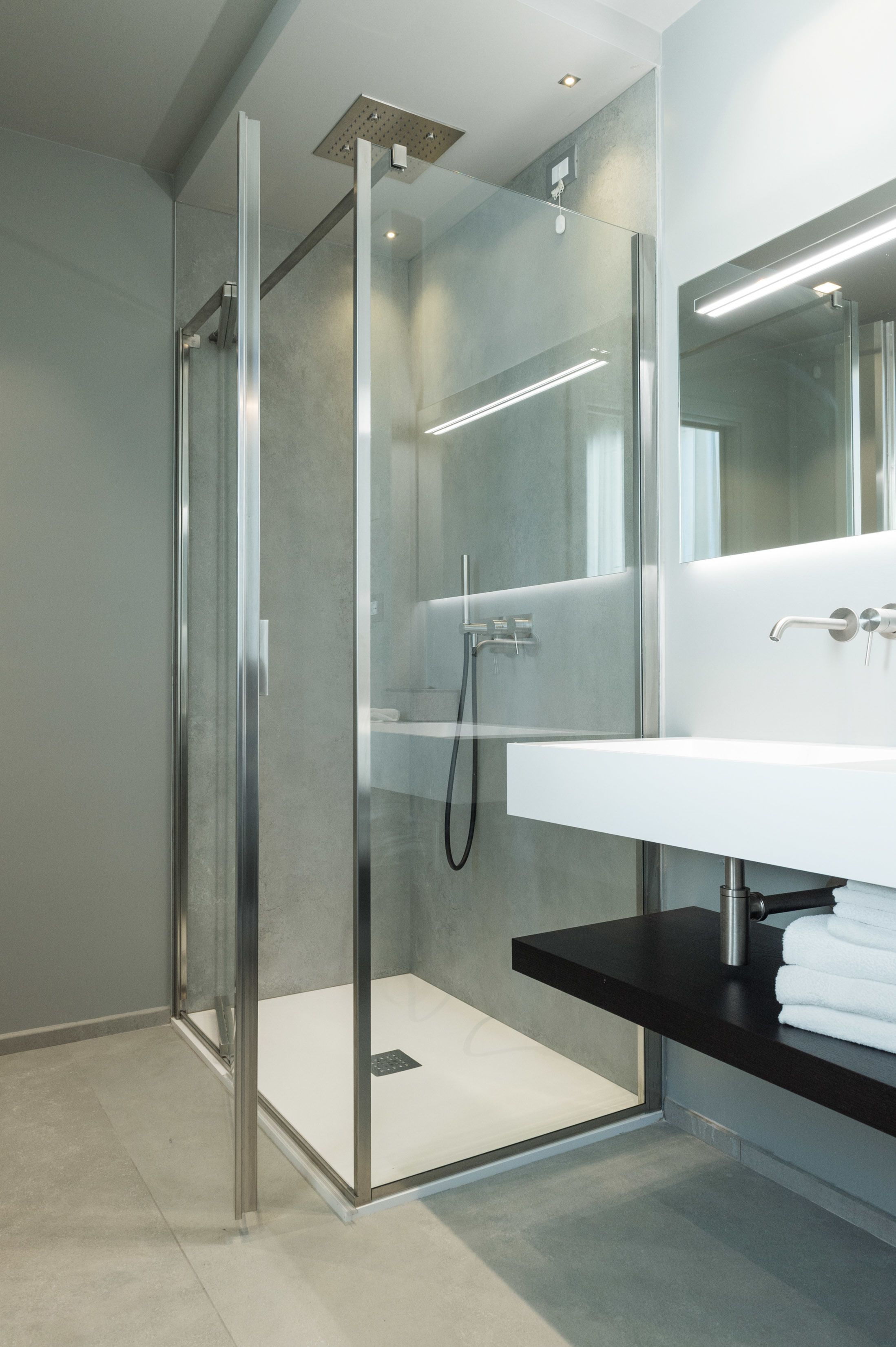 Une salle de bain moderne avec une douche à l’italienne en verre, un lavabo blanc doté d’un plan de toilette noir et un grand miroir au-dessus du lavabo.