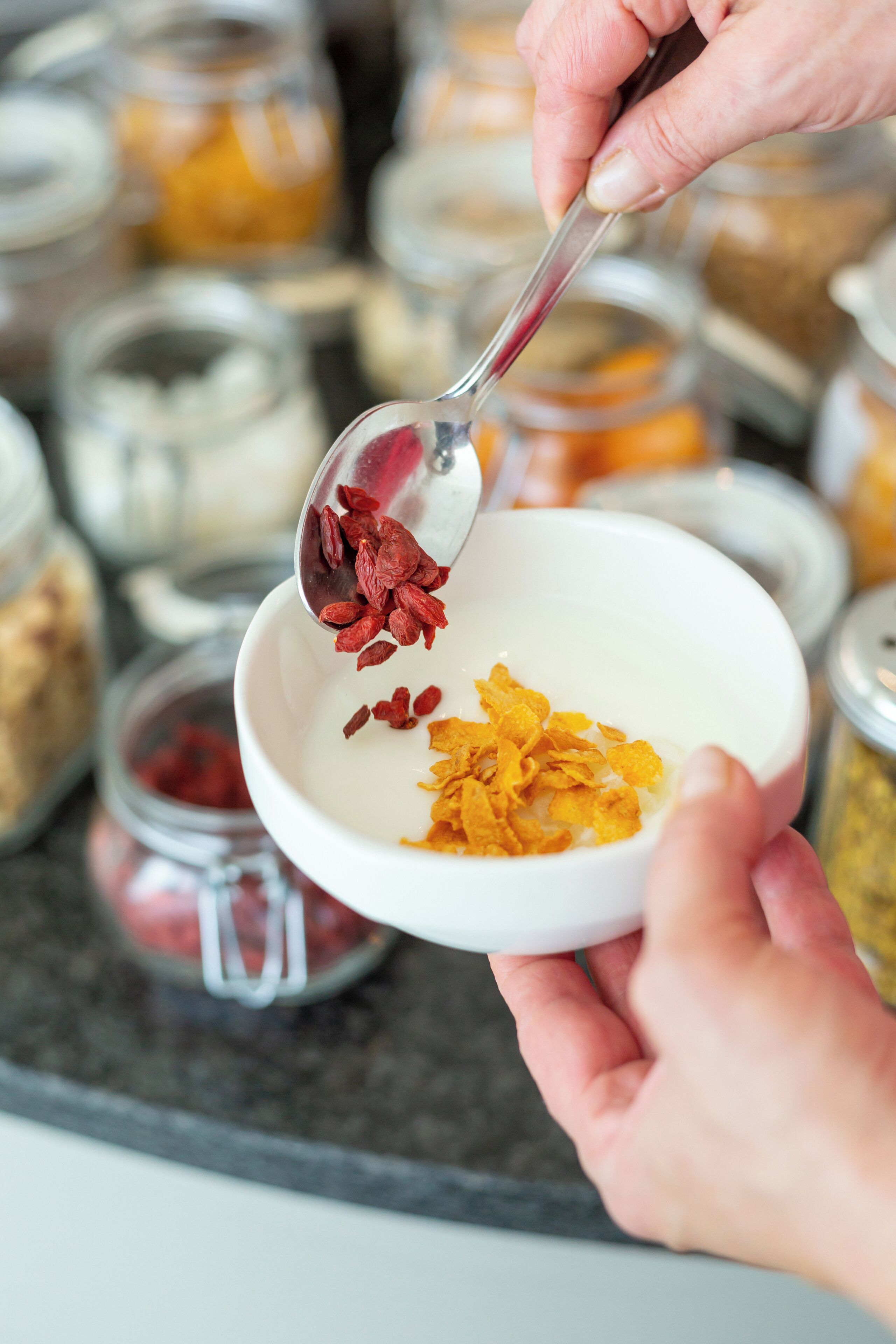 Eine Person hält einen Löffel mit roten Goji-Beeren über einer Schüssel.