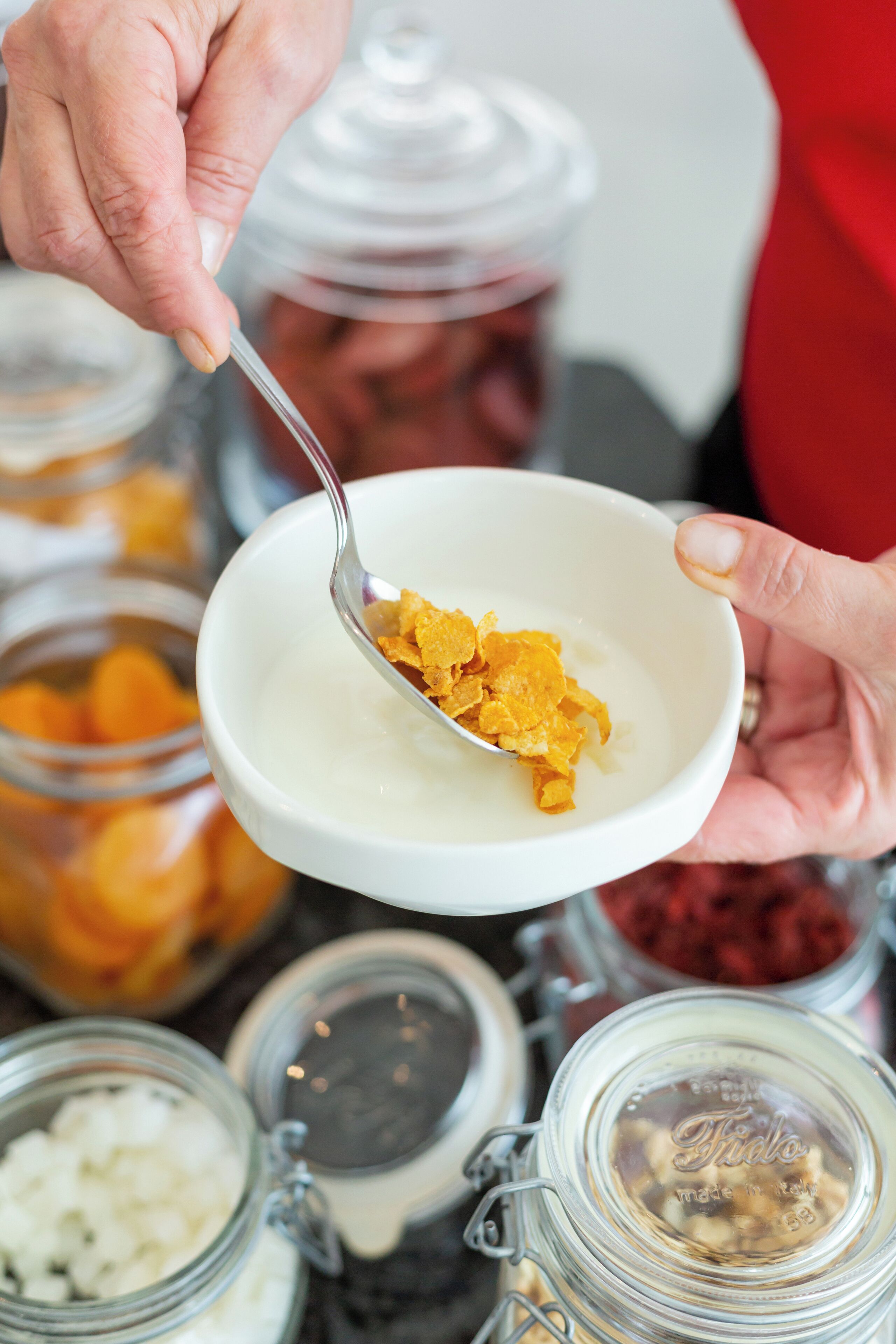 A person holding a bowl with a spoon, containing a white creamy substance and some orange flakes.