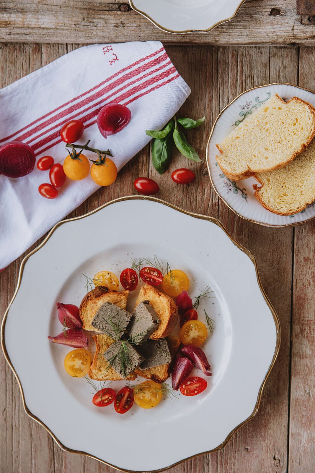 A rustic wooden table with a plate of food, a cloth with red stripes, and a plate with bread.