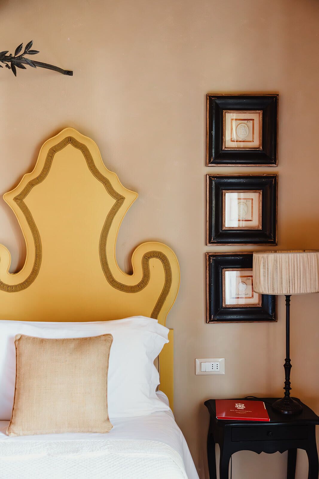 Un letto con testiera decorativa, una lampada da comodino e tre quadri appesi al muro.