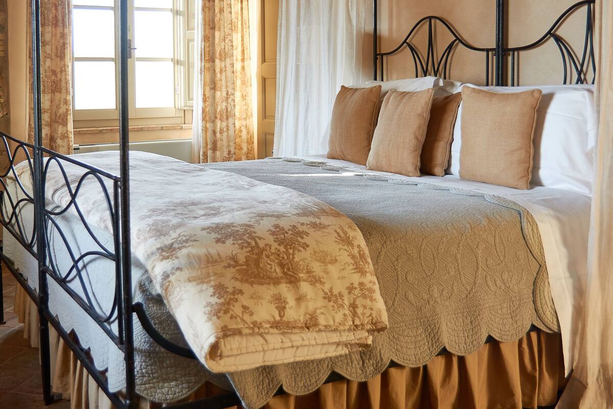 A four-poster bed with a canopy, a window with curtains, and a tiled floor.