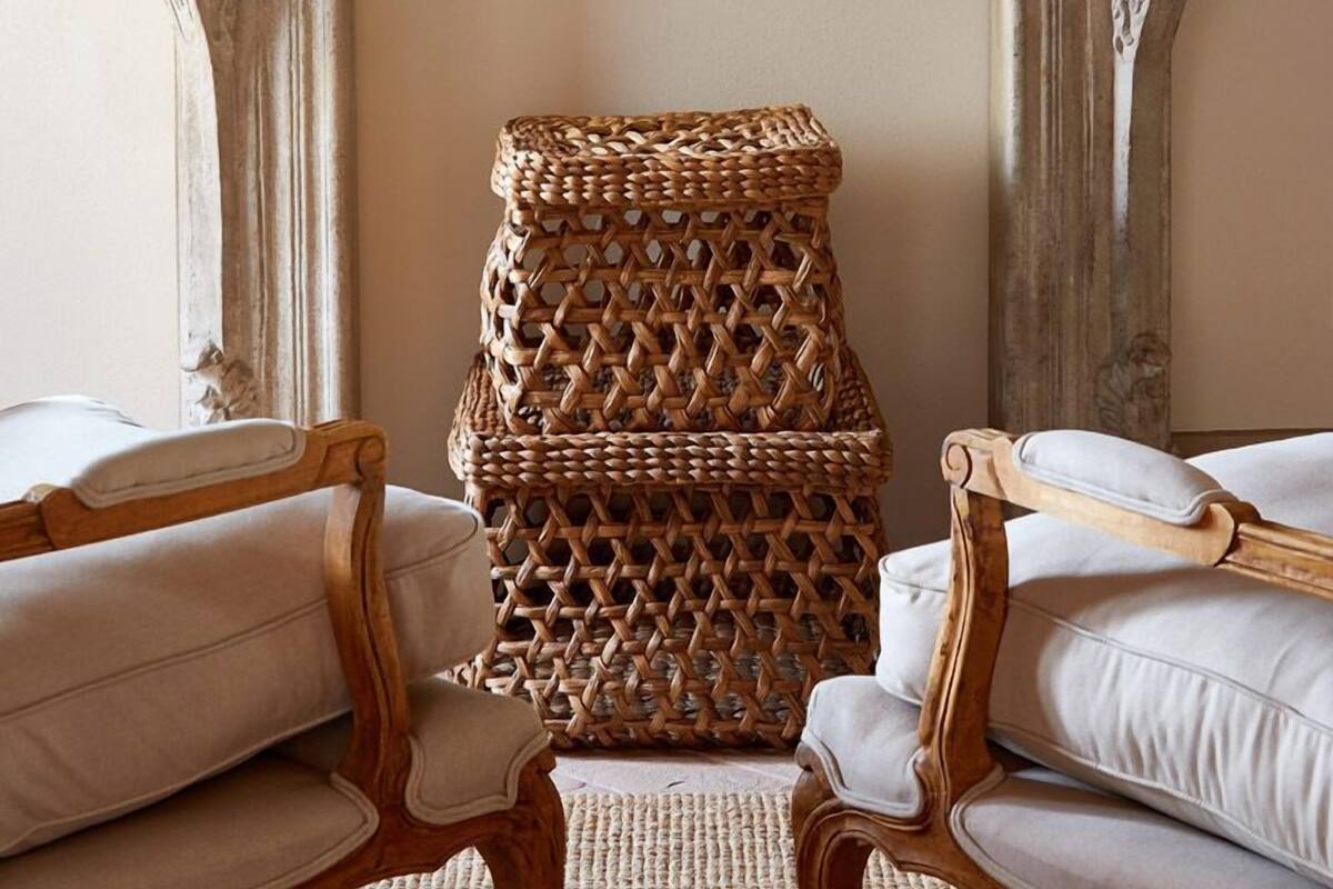 A room with a fireplace, two lamps, a wicker chair, and two sofas.