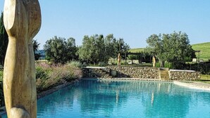 A swimming pool with a stone border, surrounded by greenery and a large sculpture. - Relais Sant'Elena (Bibbona)