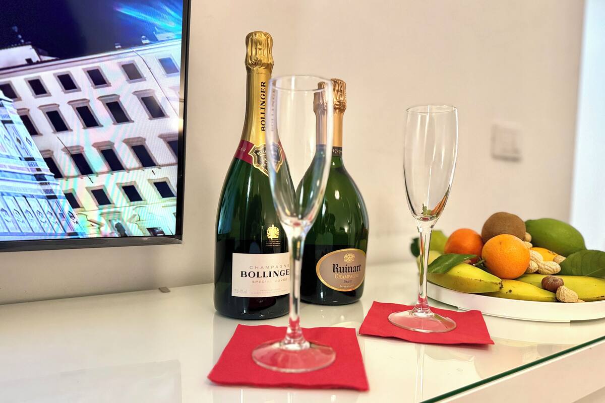 Duas garrafas de champanhe Bollinger e dois copos sobre uma mesa com um prato de frutas.