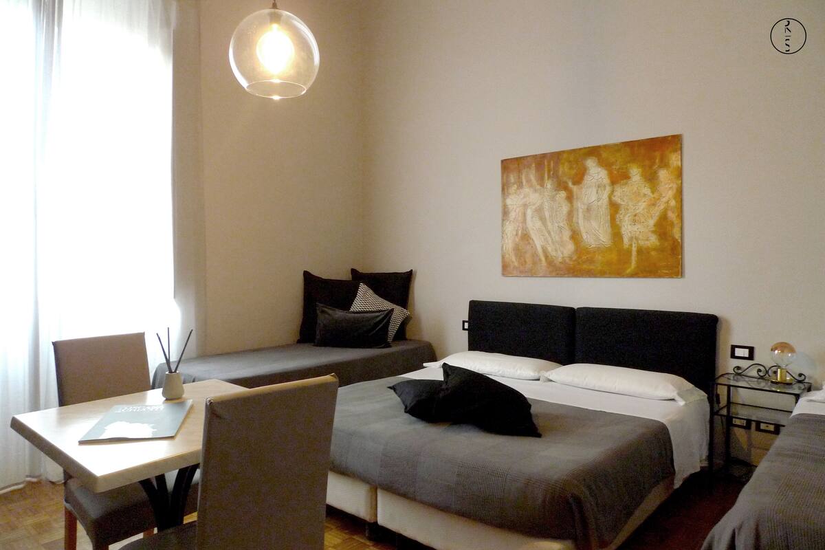 Quarto de hotel com duas camas, uma escrivaninha, uma cadeira, um abajur e um quadro na parede.