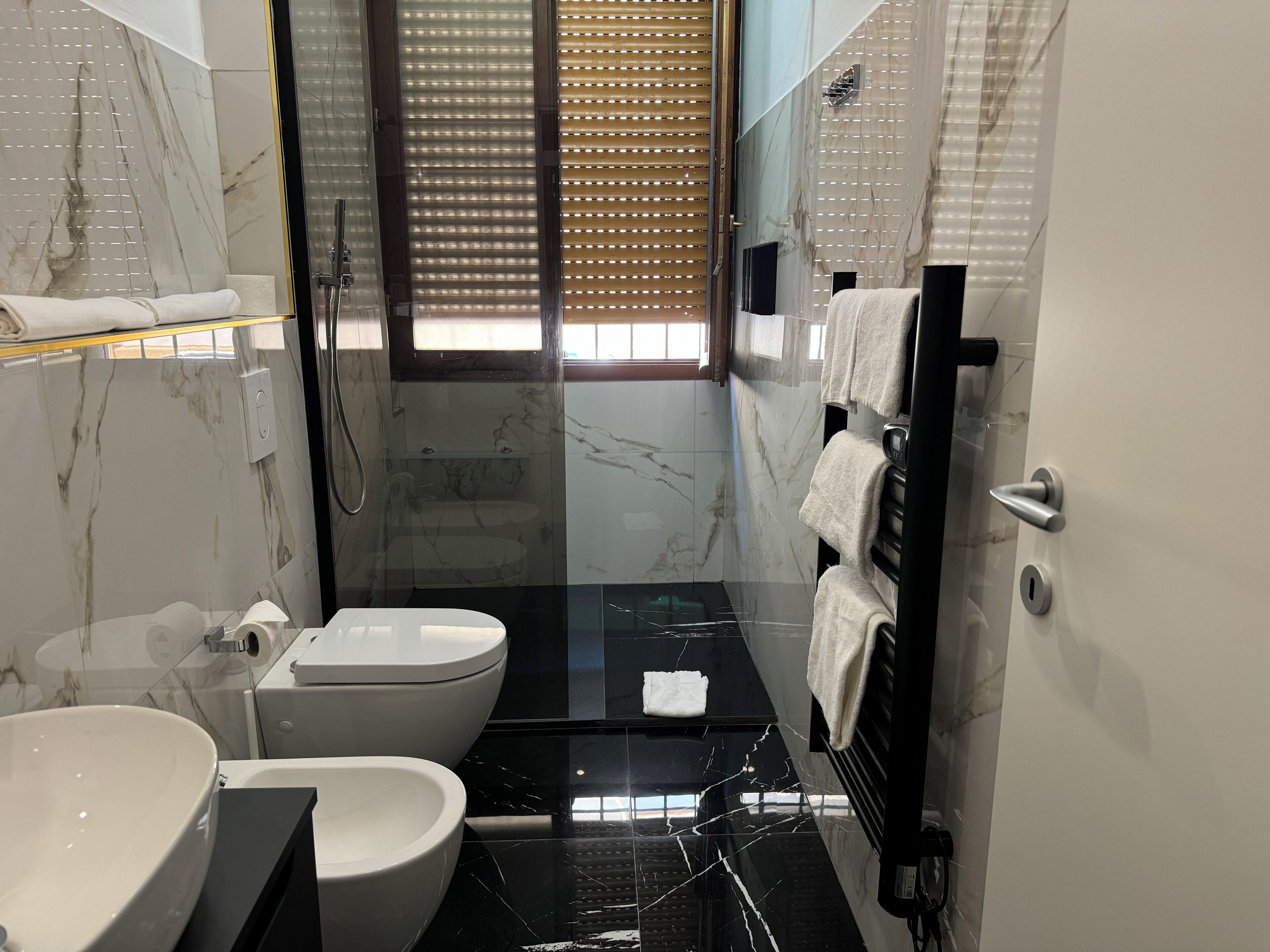 Un baño moderno con un lavabo de mármol negro, un inodoro blanco y una zona de ducha con mampara de cristal.