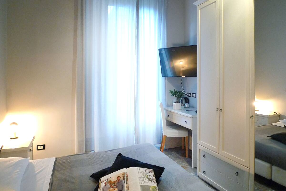 Quarto de hotel com cama, escrivaninha, televisão e armário.