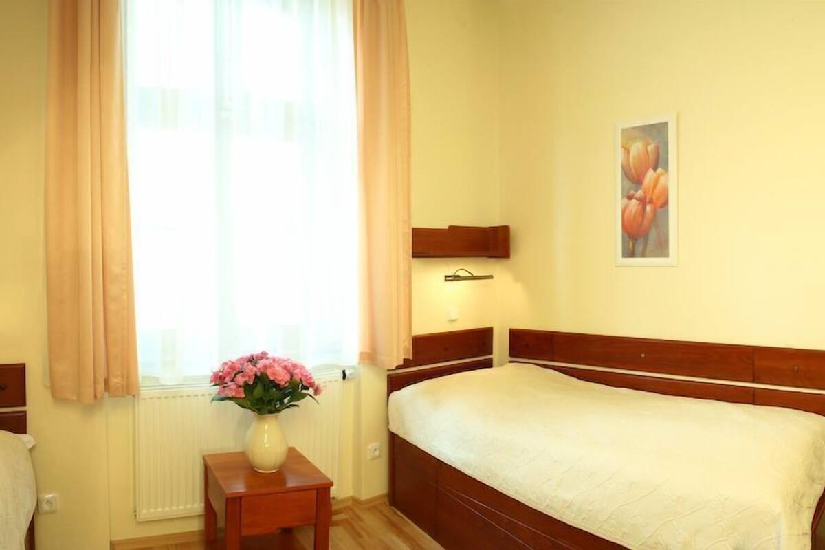 A bedroom with a bed, a nightstand, a vase with flowers, a window with curtains, and a painting on the wall.