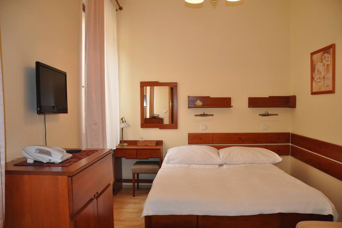 A hotel room with a bed, a desk, a chair, a telephone, a mirror, and a television.