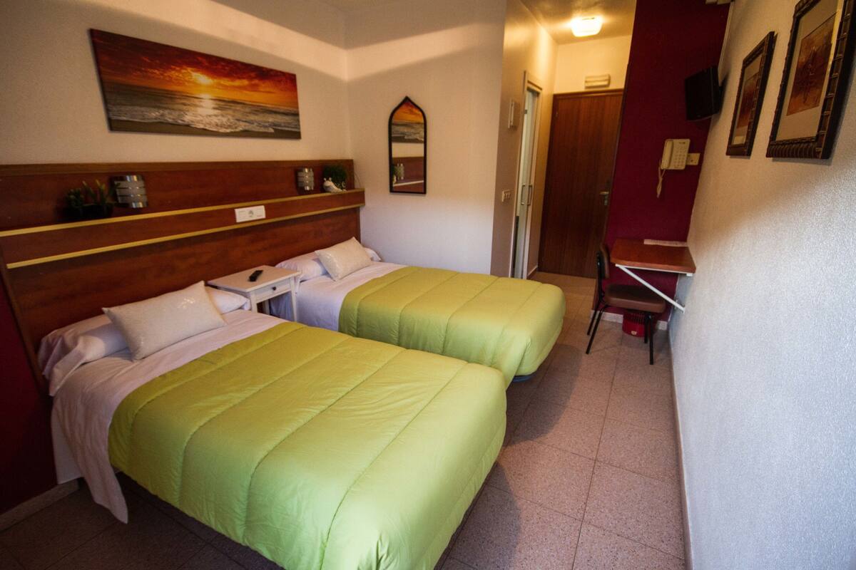 Una habitación de hotel con dos camas, un escritorio, una silla y un cuadro en la pared.