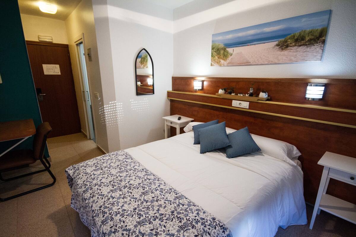 Habitación de hotel con cama, escritorio, silla, mesita de noche, espejo y decoración de pared con temática playera.