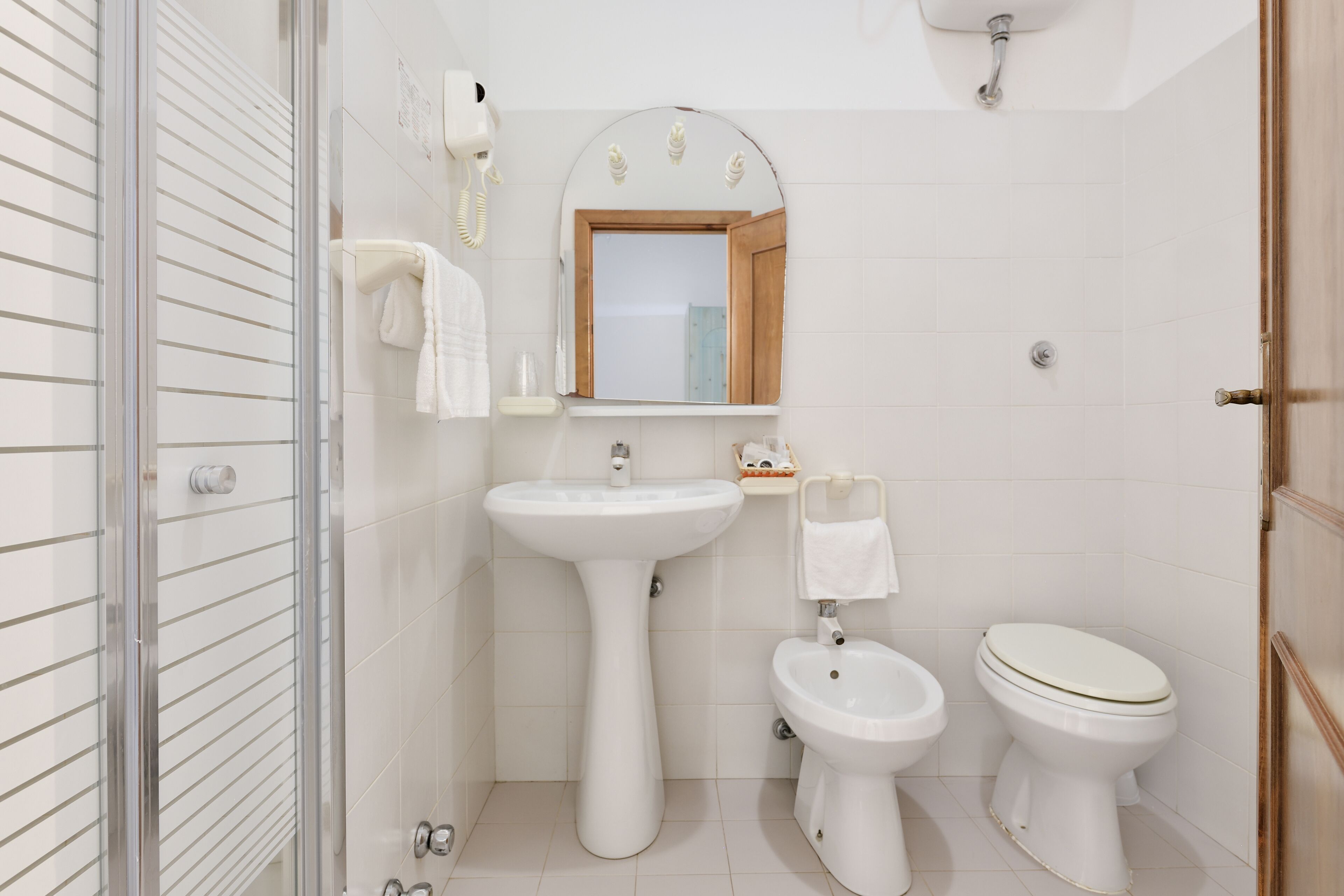 A modern bathroom with a glass shower enclosure, a pedestal sink, a bidet, and a toilet.