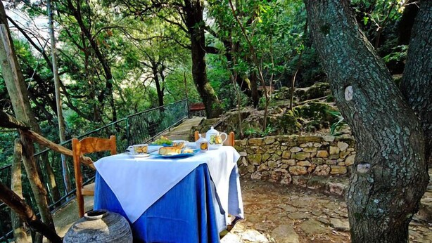 Un área de comedor al aire libre con una mesa dispuesta para dos personas, rodeada de muros de piedra y árboles.