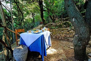 An outdoor dining area with a table set for two, surrounded by stone walls and trees. - Enis Monte Maccione (Oliena)