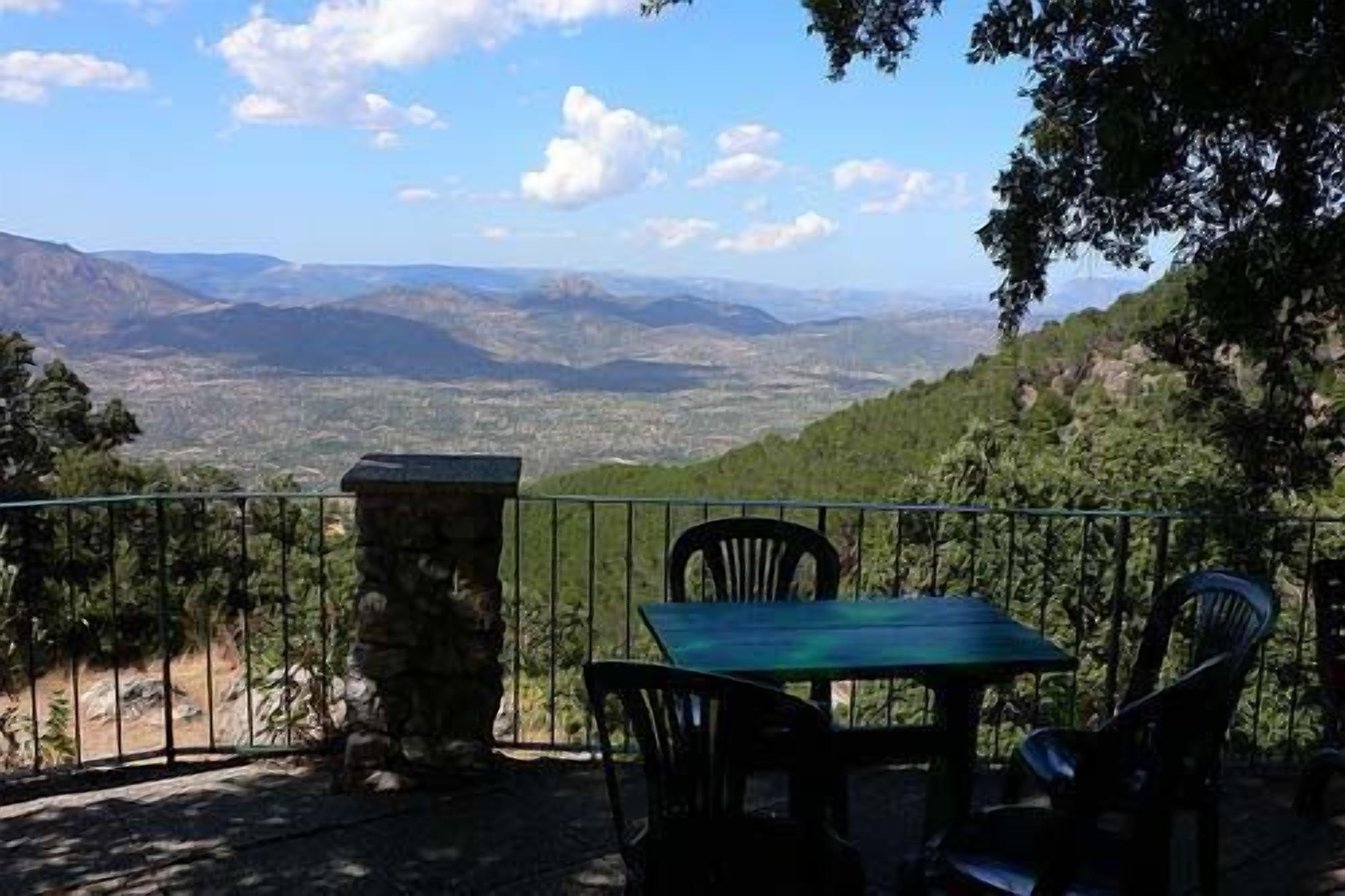 A table and chairs set on a balcony with a view of a valley and mountains.