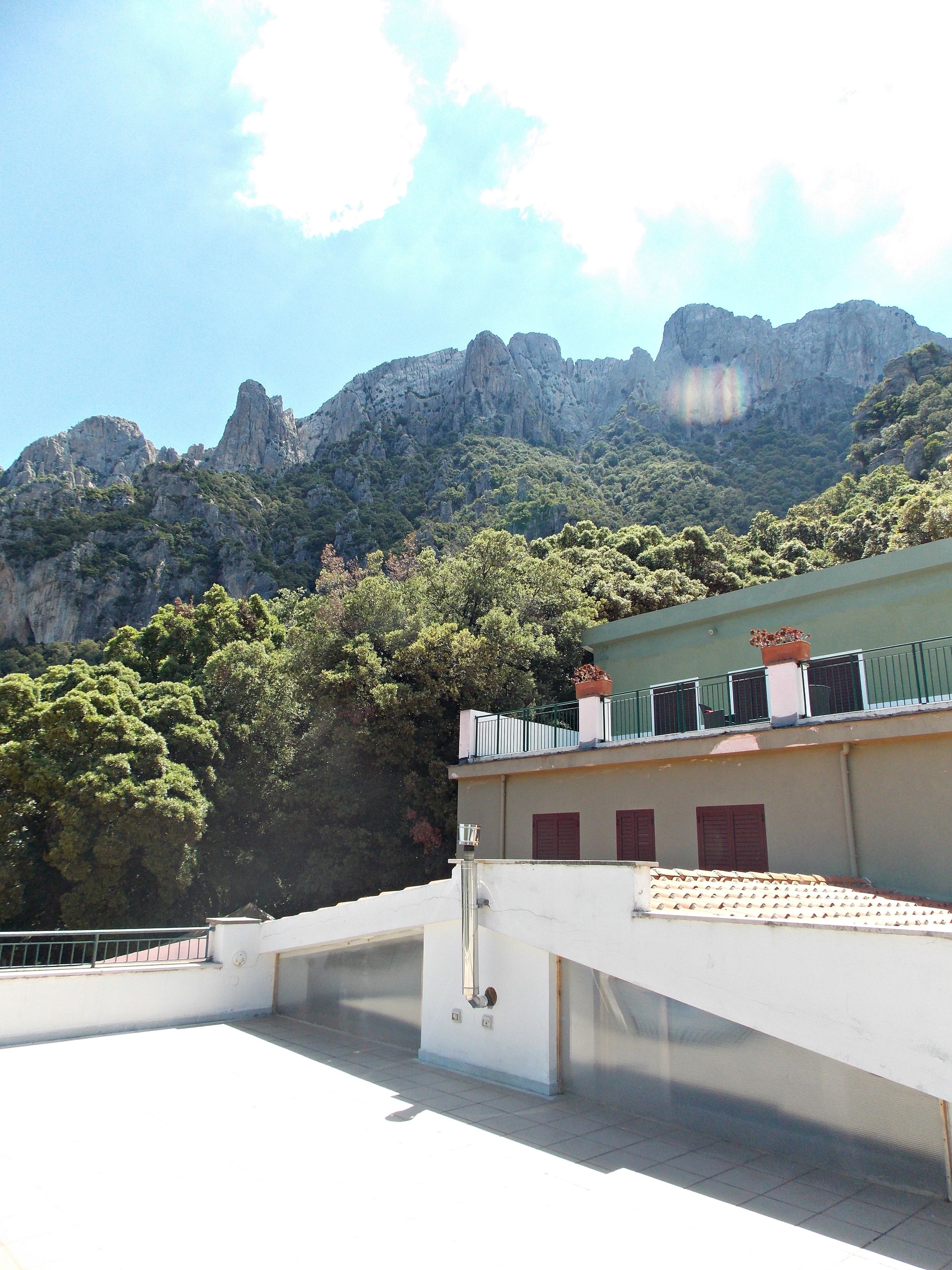 A building with a flat roof, a balcony with a railing, and a view of a mountainous landscape.