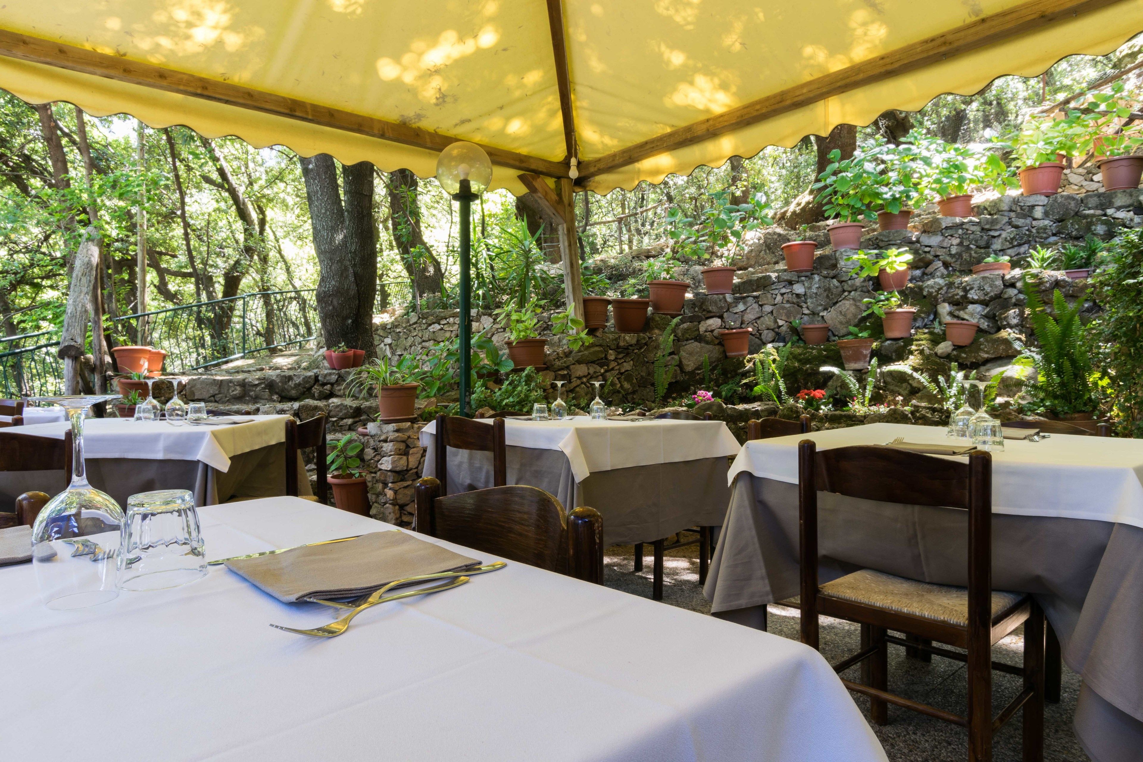 An outdoor dining area with tables set for two, surrounded by stone walls and potted plants.