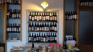 Una vitrina de vinos con varias estanterías llenas de botellas, una mesa con comida y bebidas, y un accesorio de iluminación decorativo.