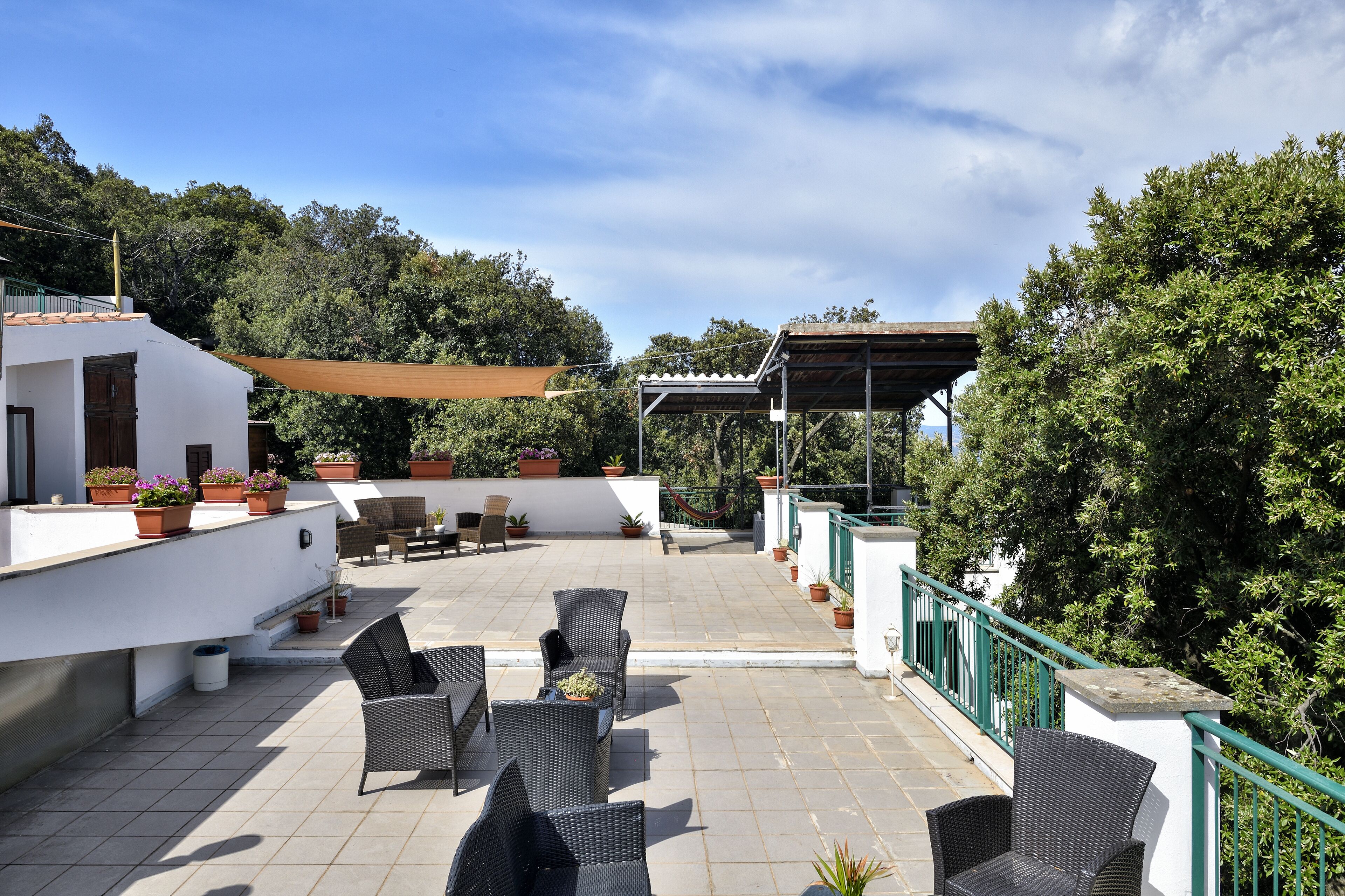 A rooftop patio with outdoor seating, potted plants, and a view of surrounding greenery.