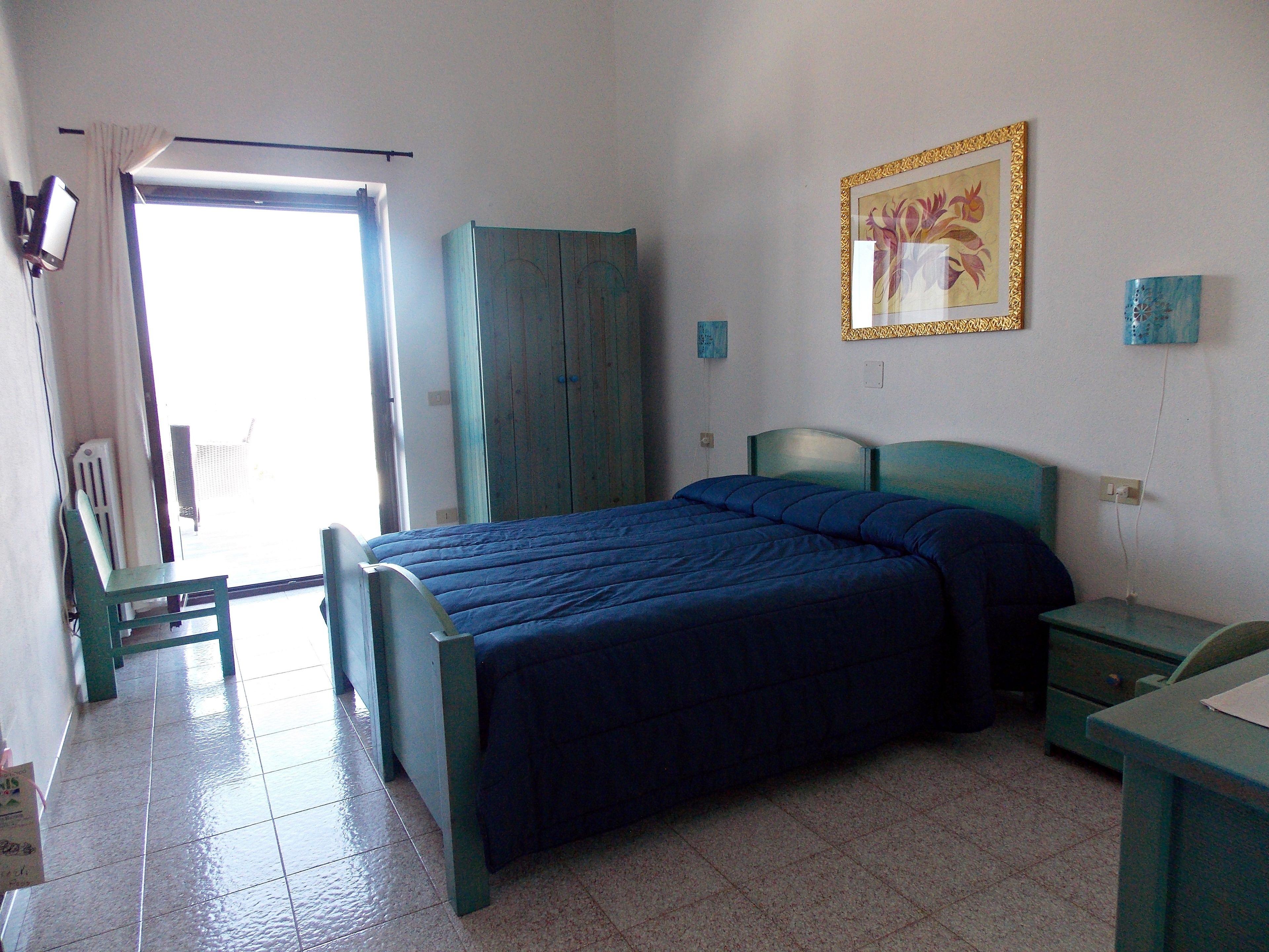 A bedroom with a bed, a chair, a desk, a wardrobe, and a window.