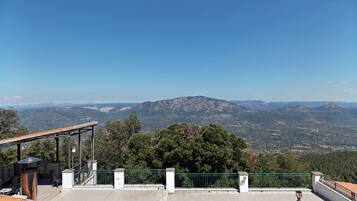 Una terraza con vista a montañas distantes, barandilla y piso de baldosas.