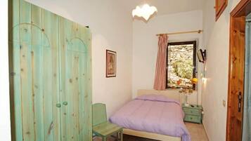 A bedroom with a bed, a chair, a wardrobe, a window with curtains, and a wall-mounted light fixture.