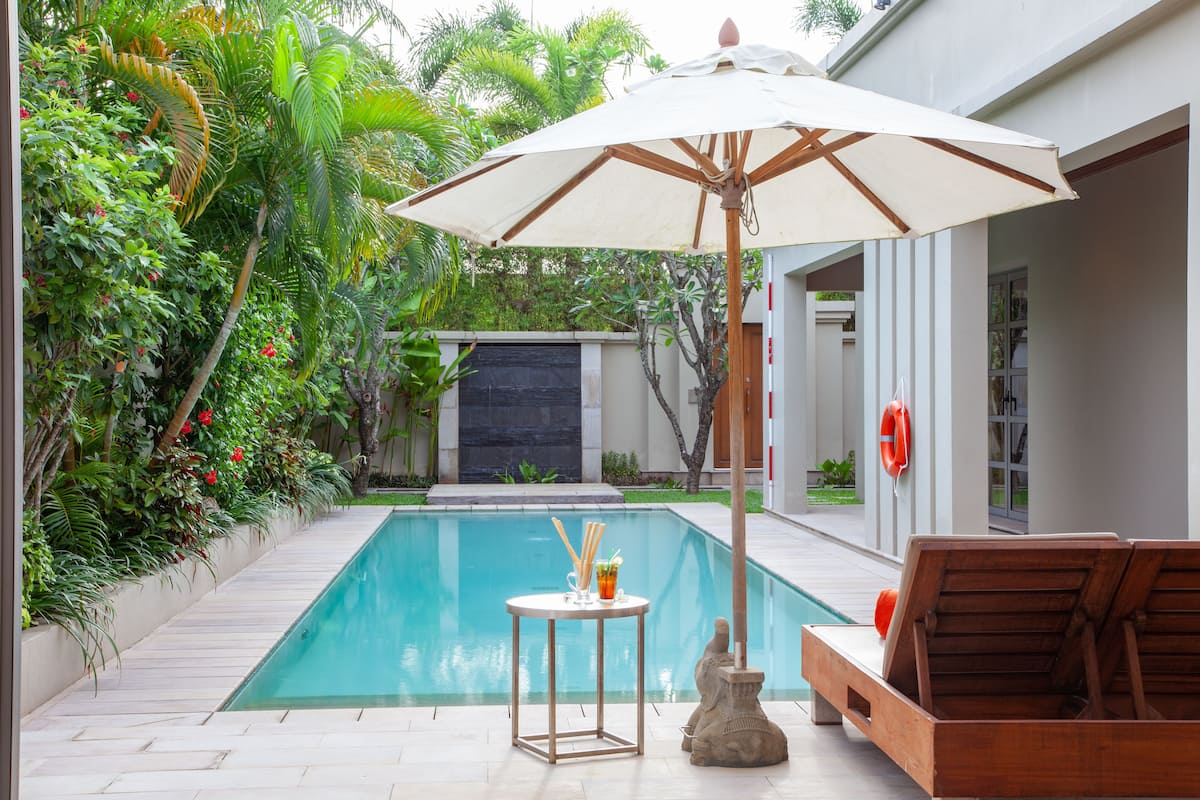 A swimming pool with a table and chairs, surrounded by lush greenery and a modern building.