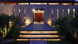 A modern building with a well-lit entrance, steps leading to a door, and a small fountain in the center.
